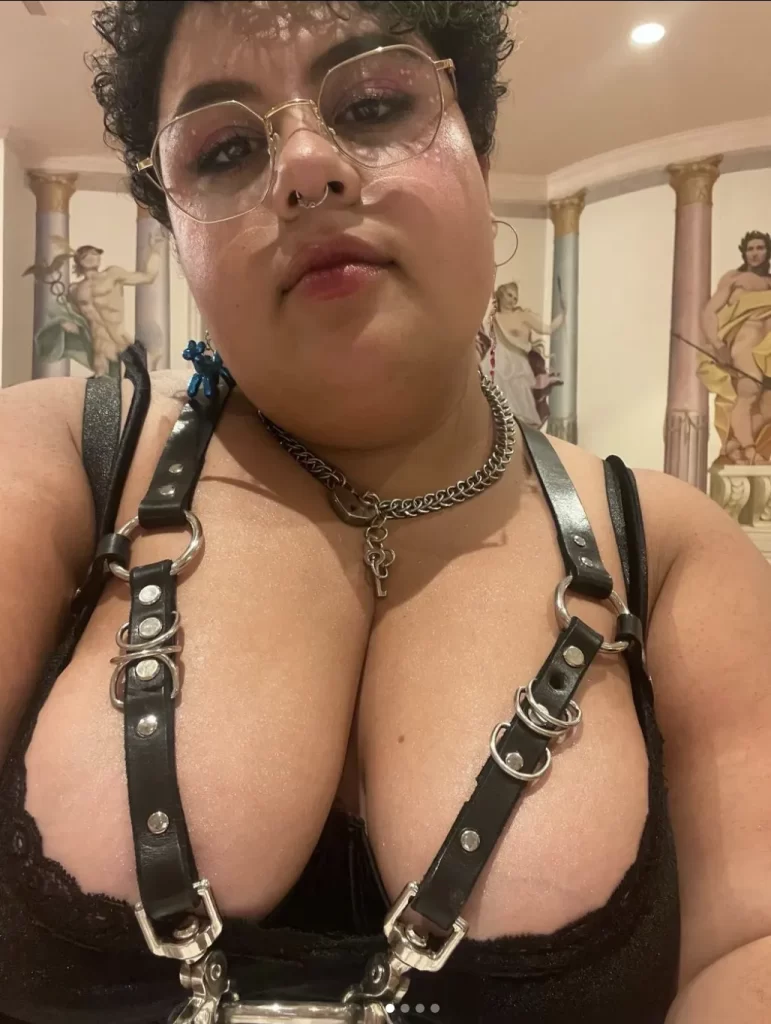 Sakina Sins, a QTPOC porn star, wearing a leather chest harness and locket necklace.